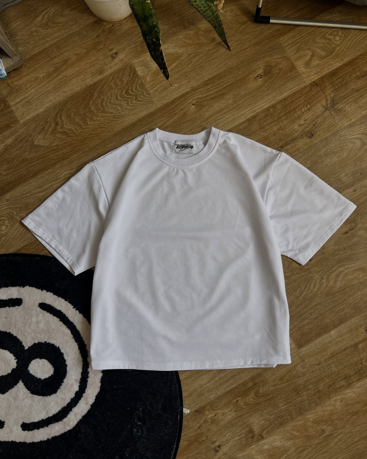 A plain white short-sleeved t-shirt lying flat on a wooden floor.