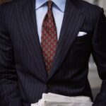 Man in a navy pinstripe suit and light blue striped shirt with a red patterned tie.