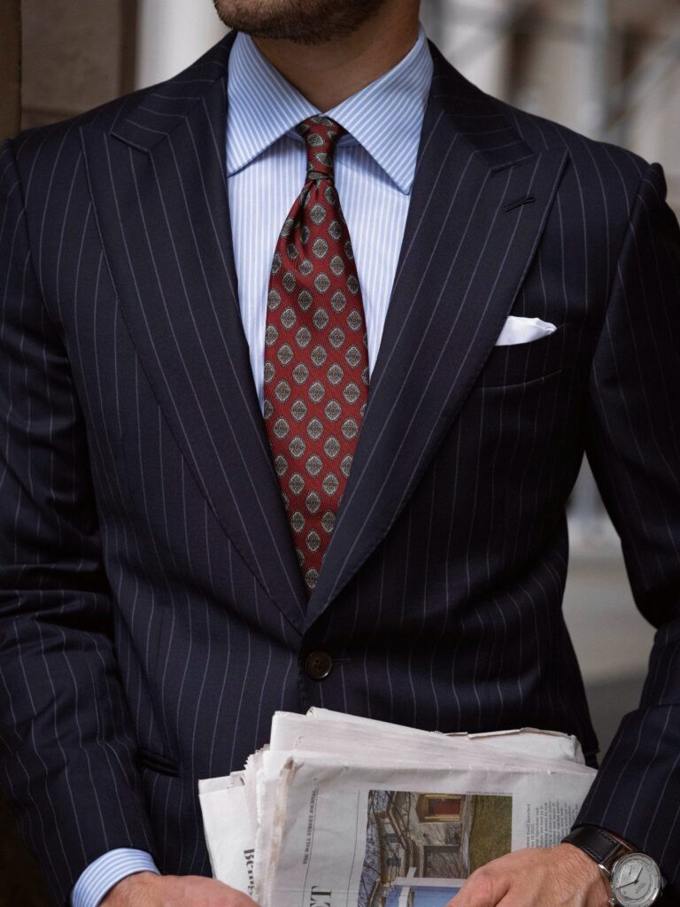 Man in a navy pinstripe suit and light blue striped shirt with a red patterned tie.