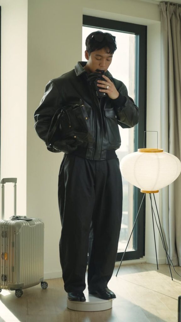 Man in an all-black outfit including a leather jacket standing in a bright room.
