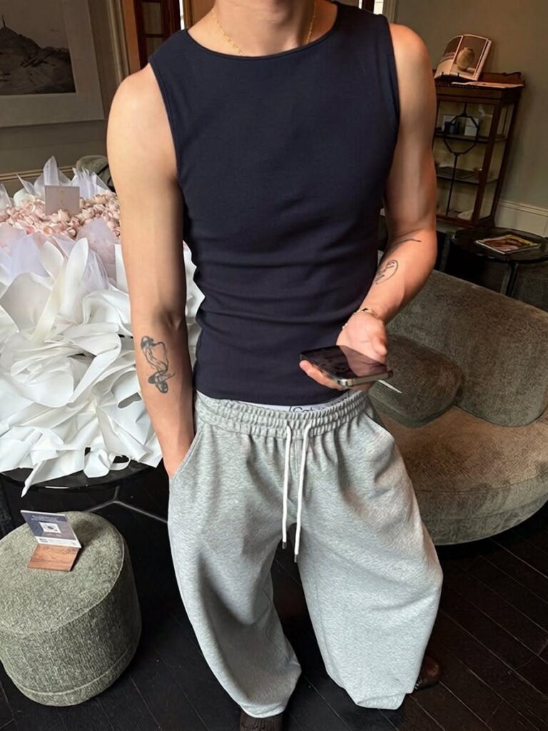 A person wearing a navy blue tank top and grey sweatpants holding a phone.