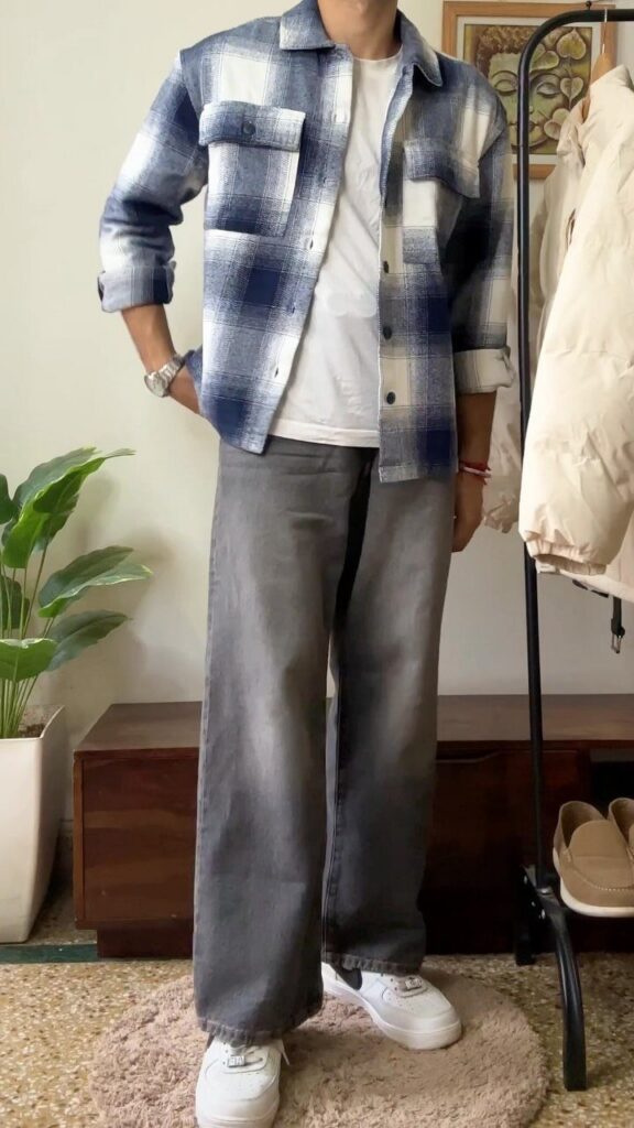 A person wearing a blue plaid shirt, white t-shirt, and grey baggy jeans with white sneakers.