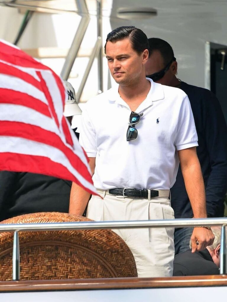 A man in a white polo shirt and light trousers standing near an American flag.