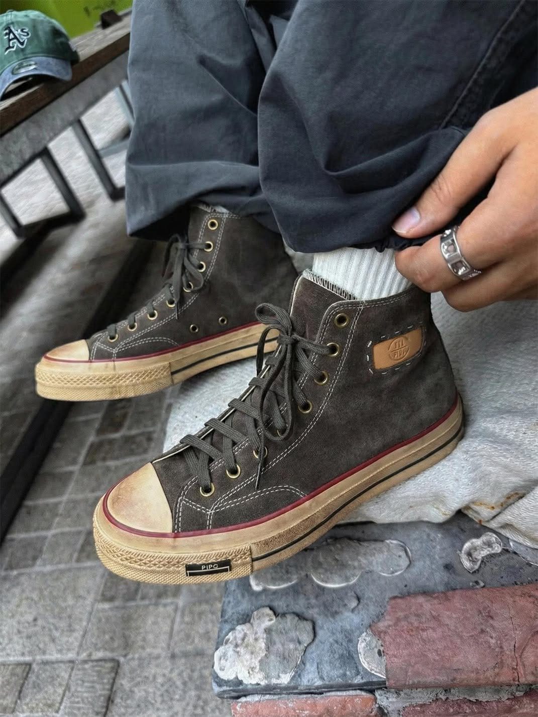 Olive green high-top canvas sneakers with red stripe soles worn with grey trousers and white socks.