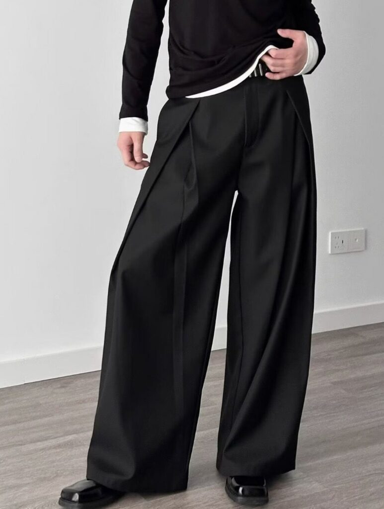 Person wearing black pleated wide-leg trousers and a black long-sleeve shirt.