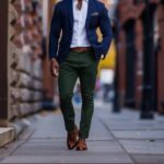 A man walking in a city wearing a navy blazer and green trousers.
