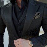 Man wearing a black patterned blazer, waistcoat, and button-down shirt with a gold watch.