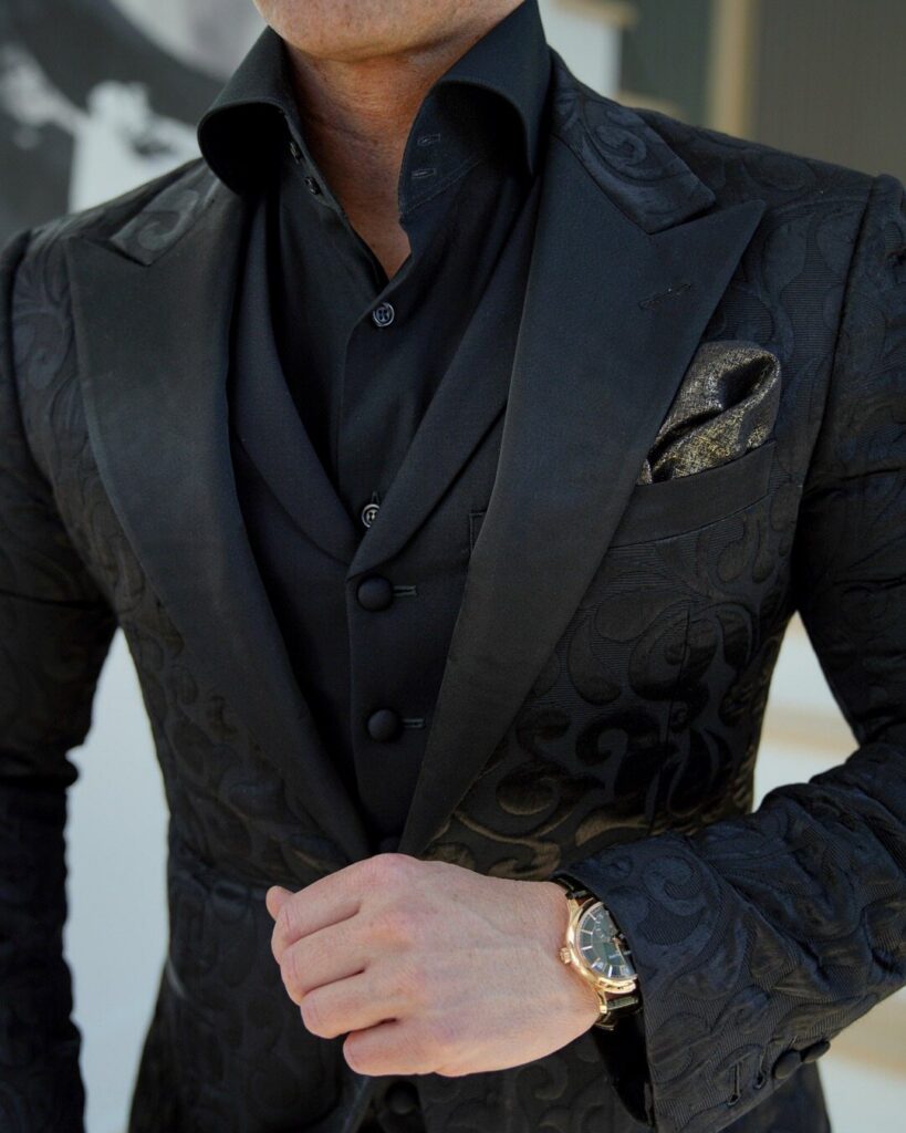 Man wearing a black patterned blazer, waistcoat, and button-down shirt with a gold watch.