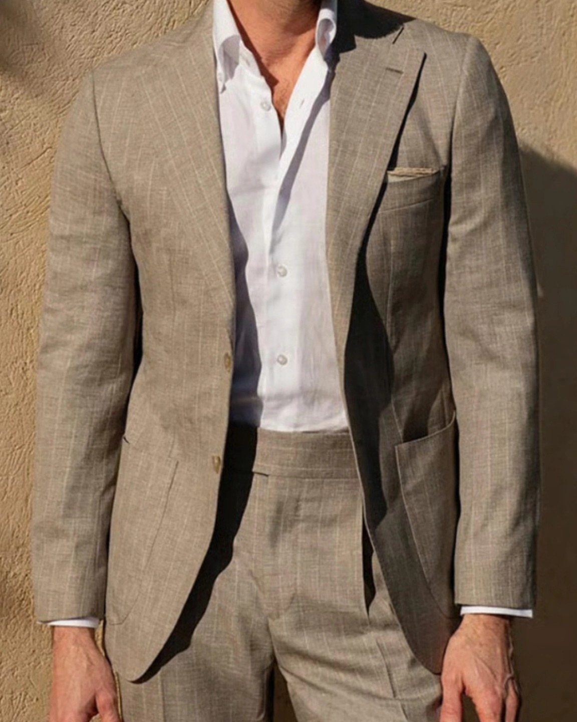 Man wearing a light beige linen suit and a white button-down shirt outdoors.