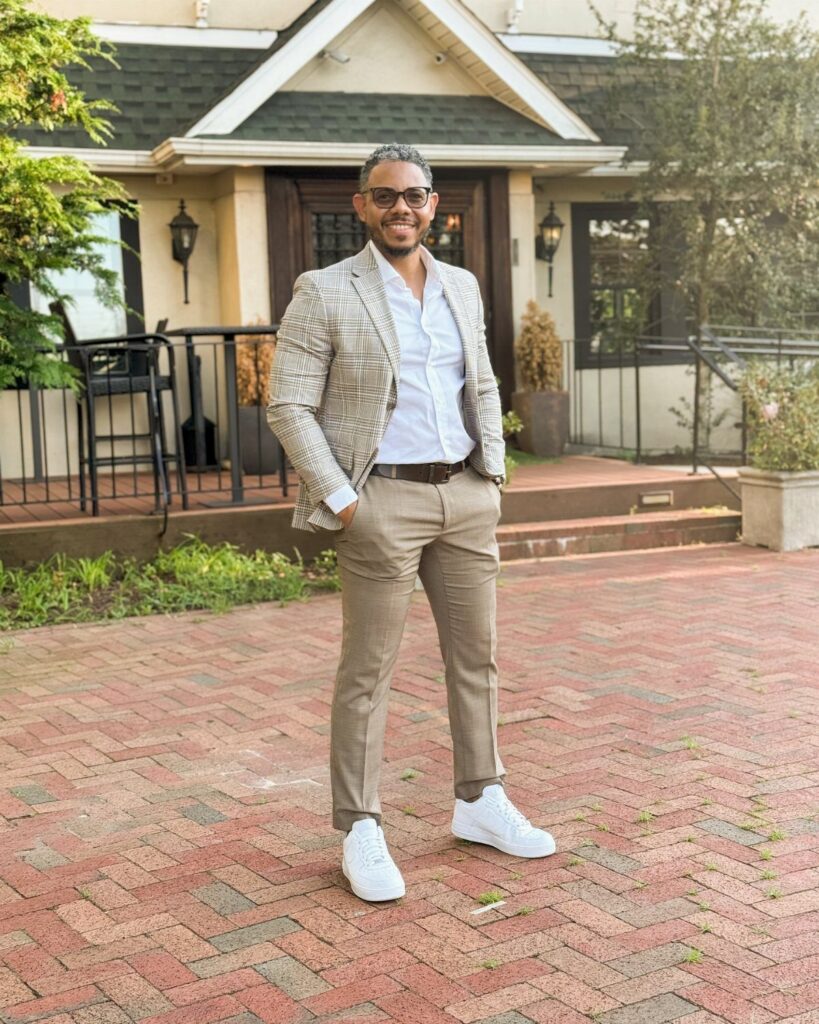 A man wearing a beige patterned blazer, white dress shirt, tan chinos, and white sneakers.