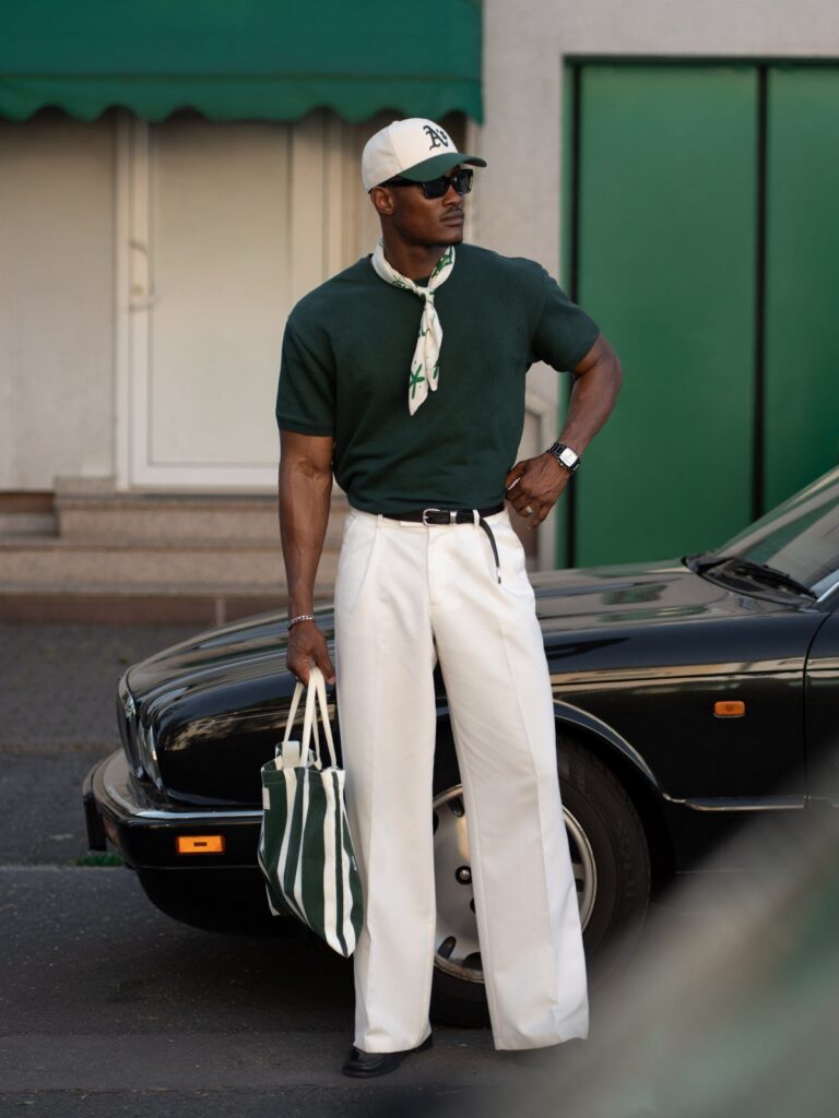Man in dark green polo and white trousers posing next to a black car.