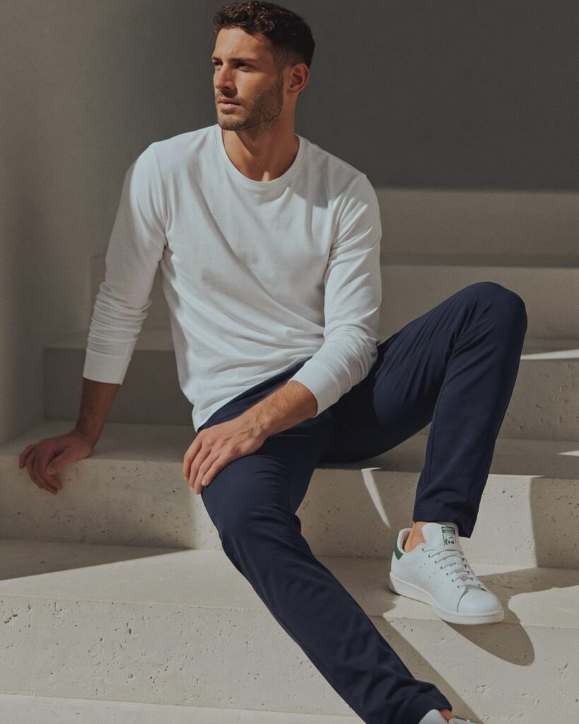 Man sitting on stone steps wearing a white long-sleeve shirt and navy slim-fit chinos.