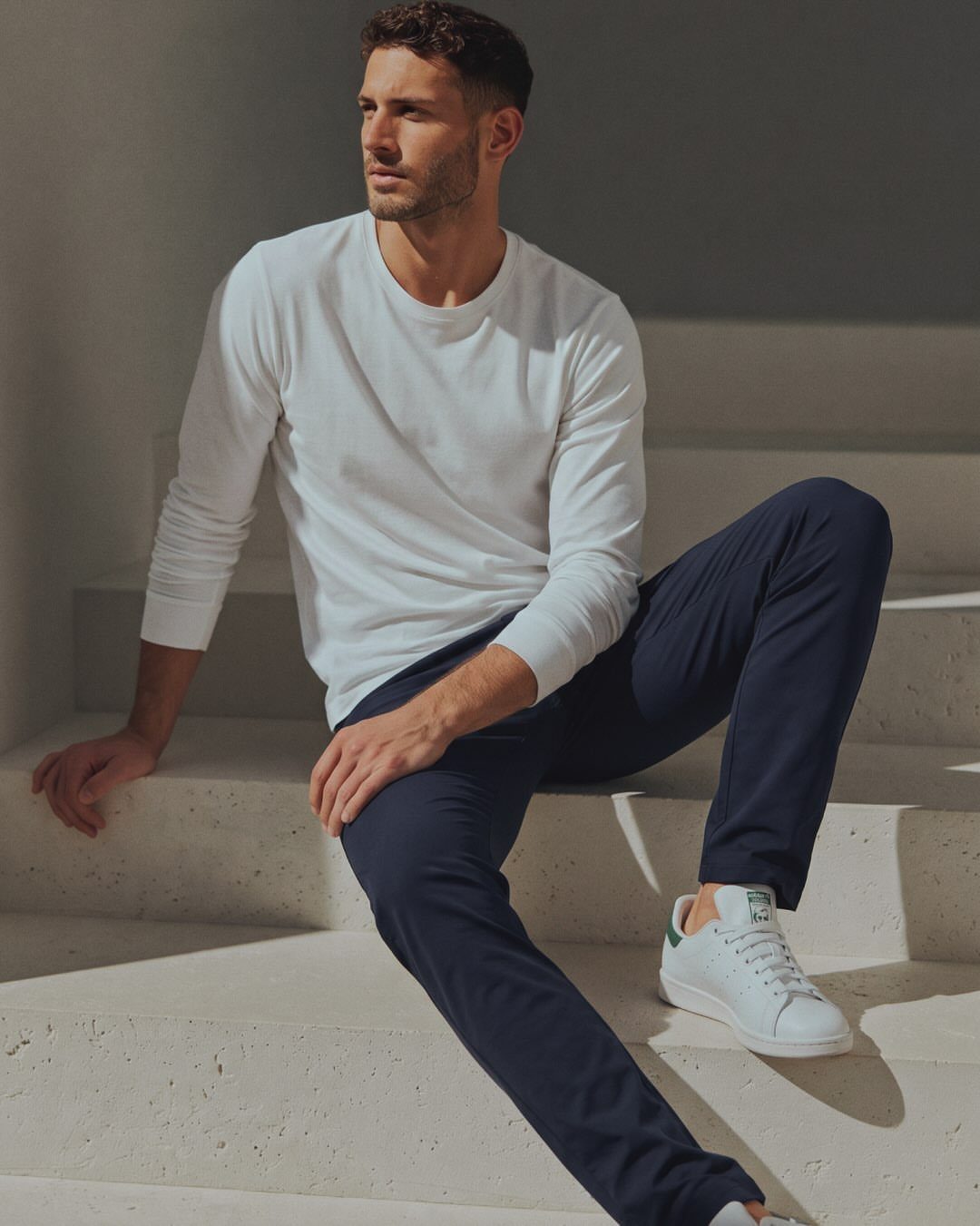 Man sitting on stone steps wearing a white long-sleeve shirt and navy slim-fit chinos.