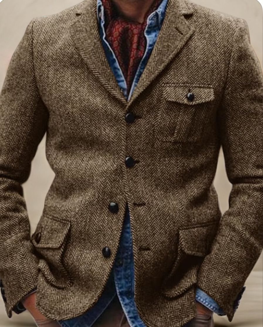 A man wearing a brown herringbone tweed blazer over a blue denim shirt and red scarf.