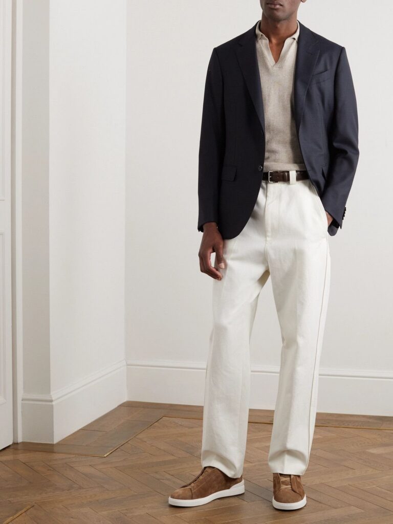 A man wearing a dark navy blazer, beige polo, and cream wide-leg trousers.