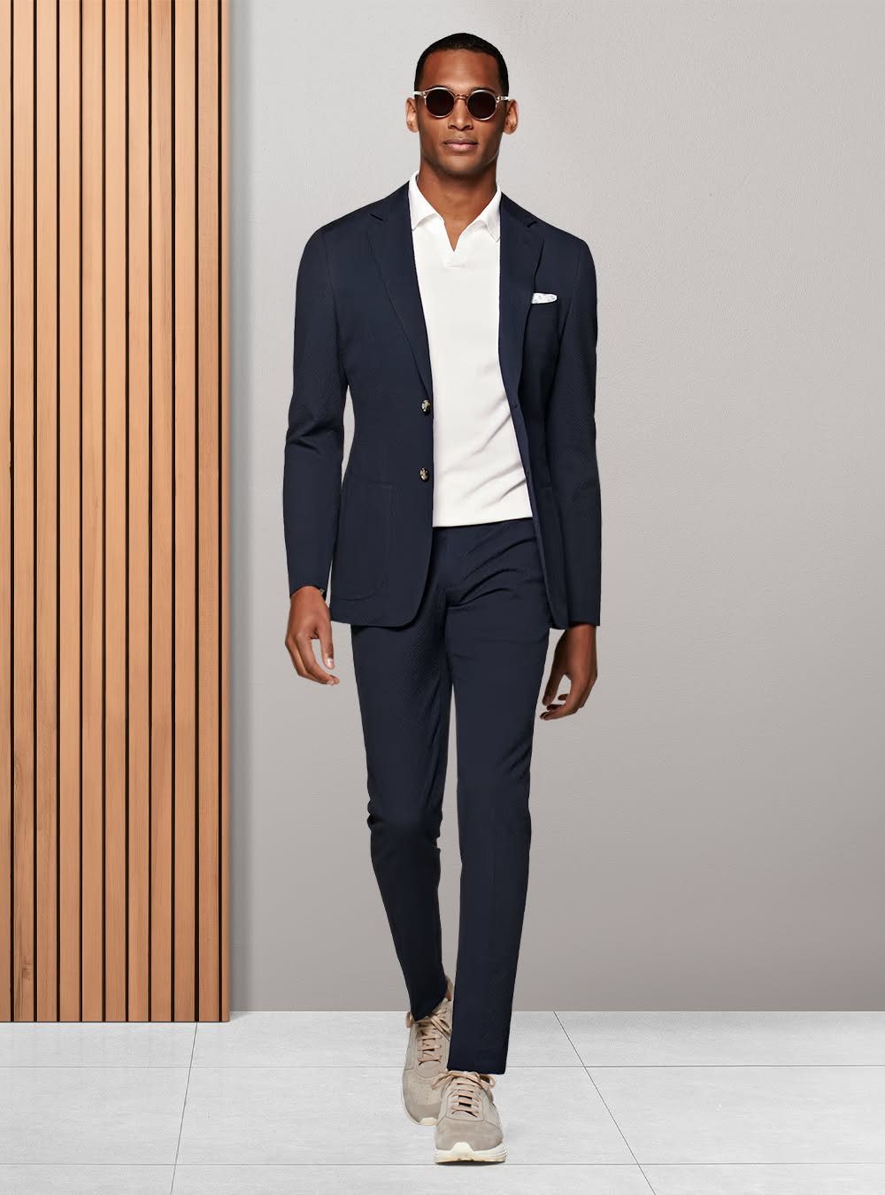 Man in a navy blue suit and white polo shirt walking outdoors.