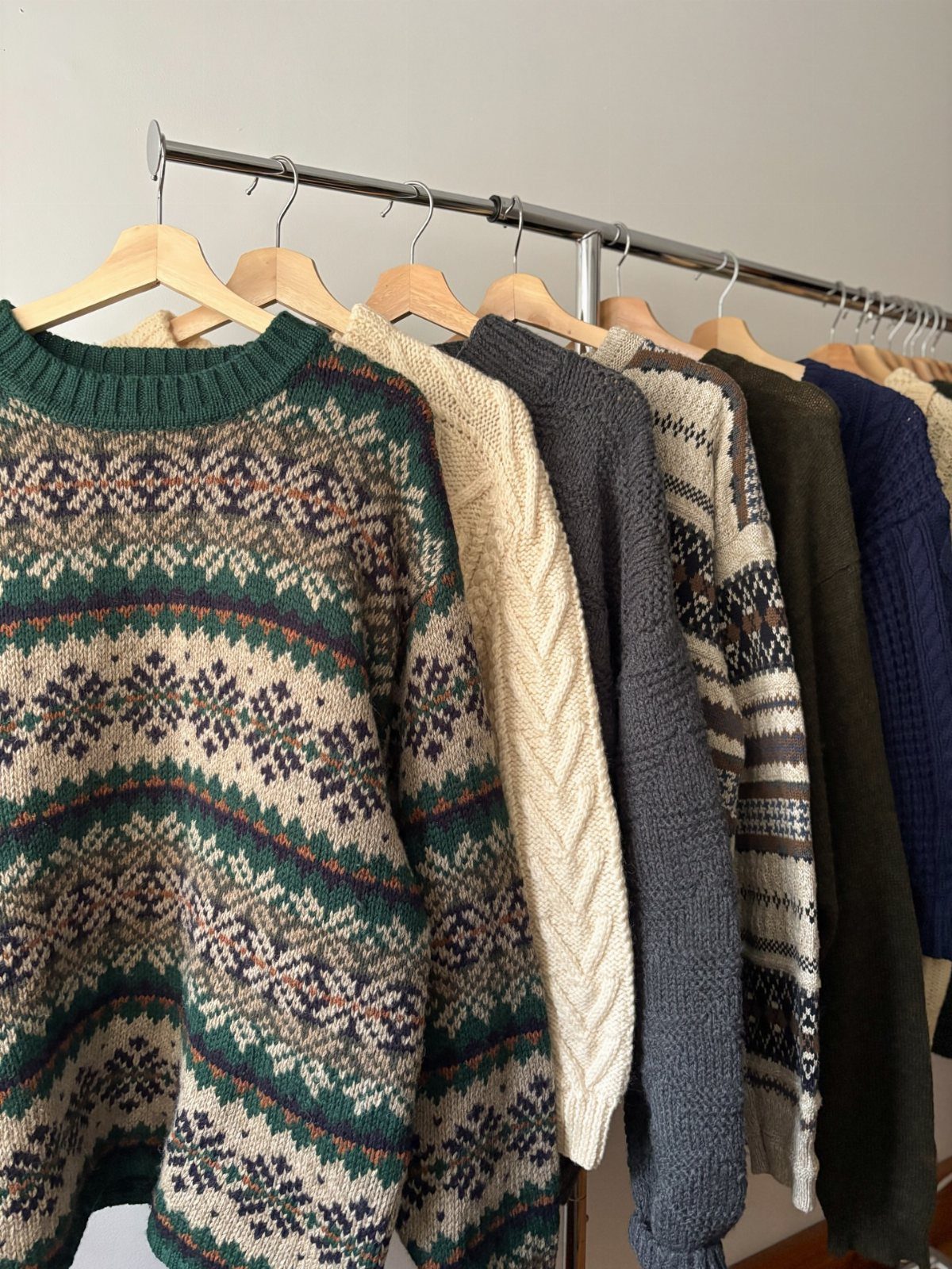 Various patterned and solid knit sweaters hanging on a metal clothing rack.